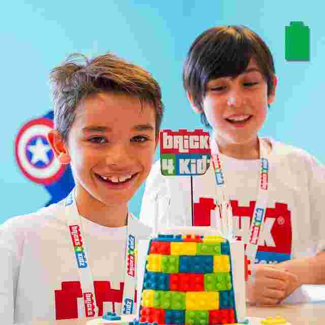 Two smiling children in "Brick 4 Kidz" shirts build a colorful LEGO structure. A superhero shield is visible in the background.