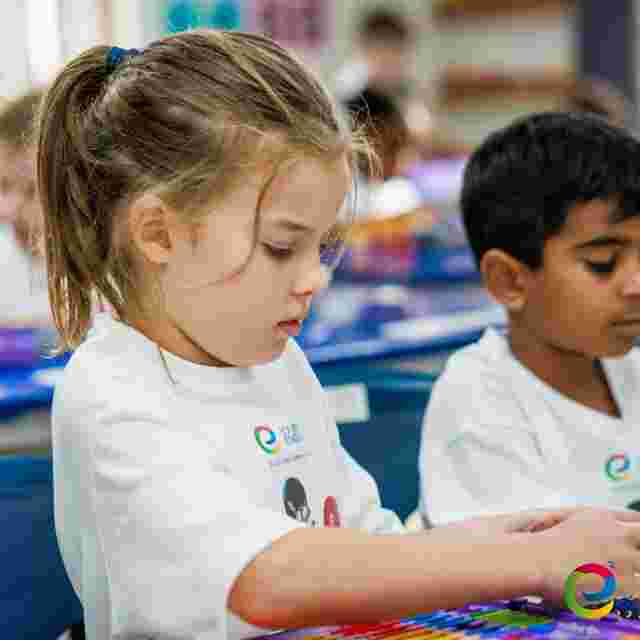 A young girl and boy in white shirts focus on colorful activities at a classroom table, surrounded by educational materials.