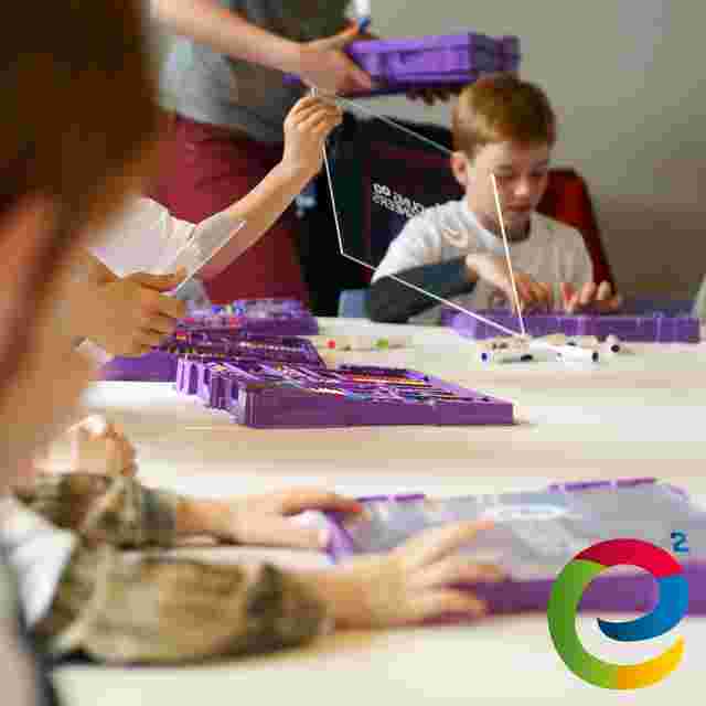 Children engaged in a hands-on educational activity with purple Young Engineers LEGO kits on a table, featuring a colorful logo in the corner.