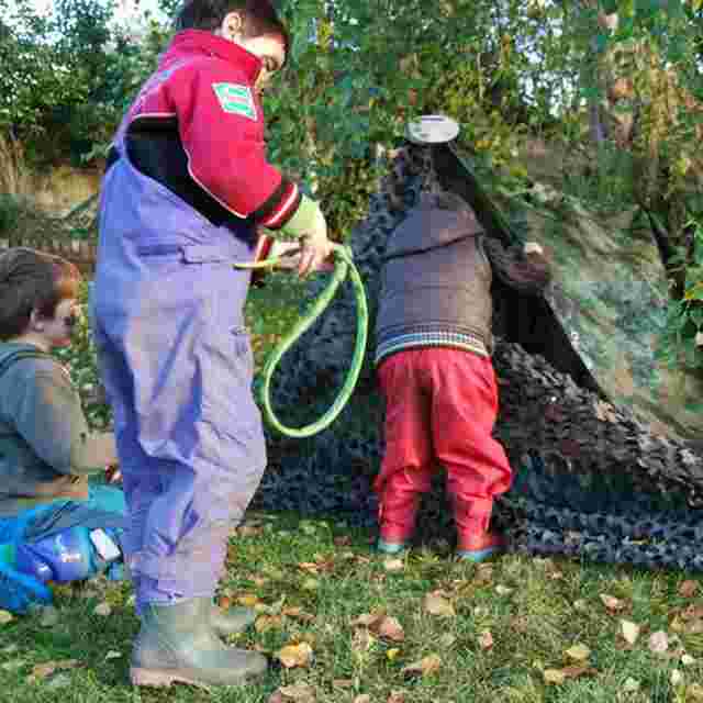 Three children outside building a shelter using tarps and camouflage materials
