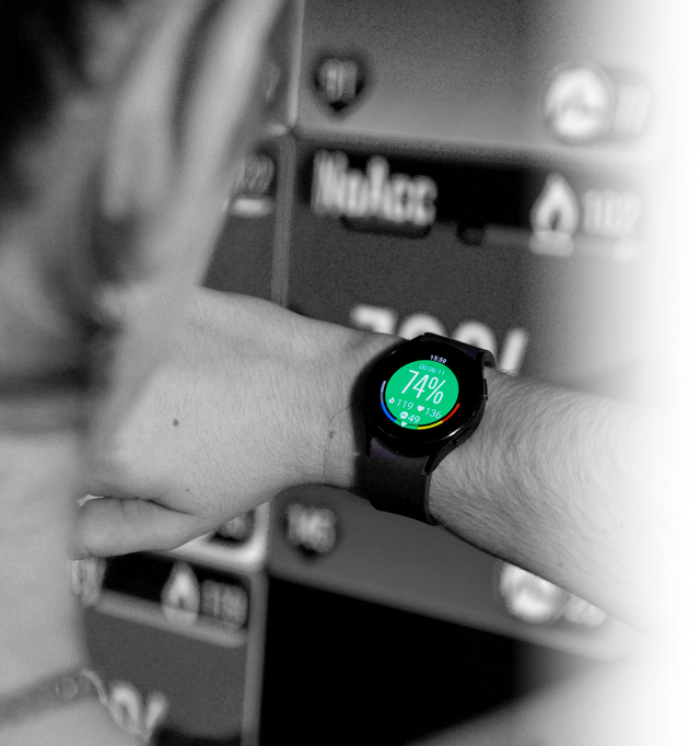 Person checking a smartwatch displaying 74% effort against a blurred background of digital icons.