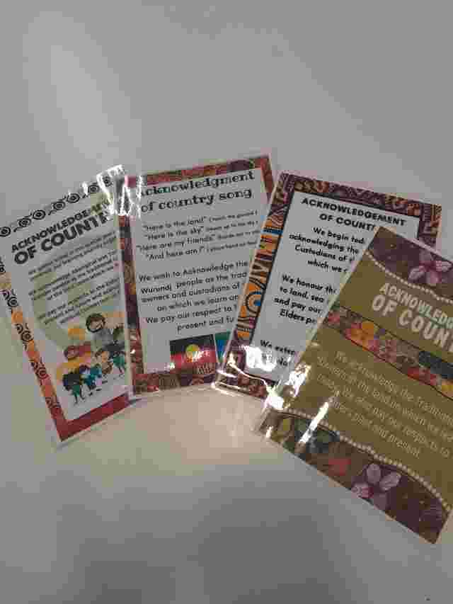 Laminated cards with "Acknowledgment of Country" text, featuring colorful borders and illustrations, laid out on a white surface.