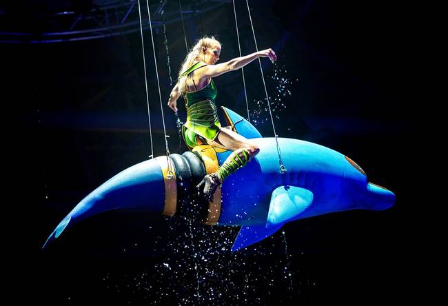 live show with woman in a green suit sitting on a blow up dolphin floating in the air
