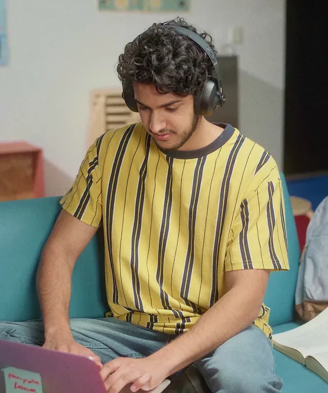 Man on a sofa with laptop and over-ear headphones, using licensed music for a creative project.