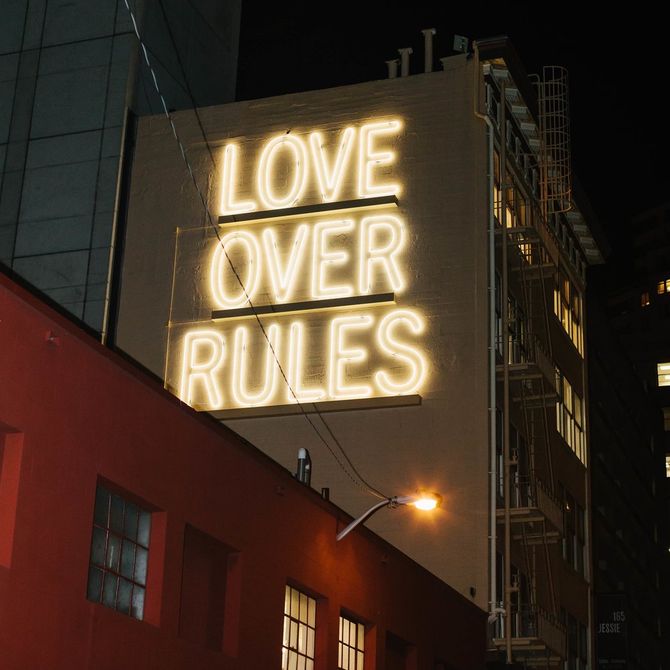 Large neon lighting spelling out 'LOVE OVER RULES' on the side of a tall building 