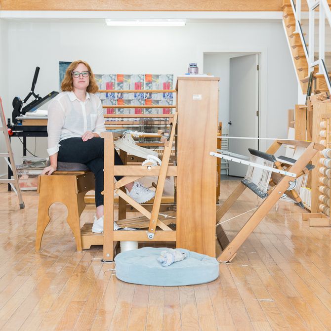 Margo Wolowiec sat at a wooden weave in her studio next to a staircase looking towards the camera