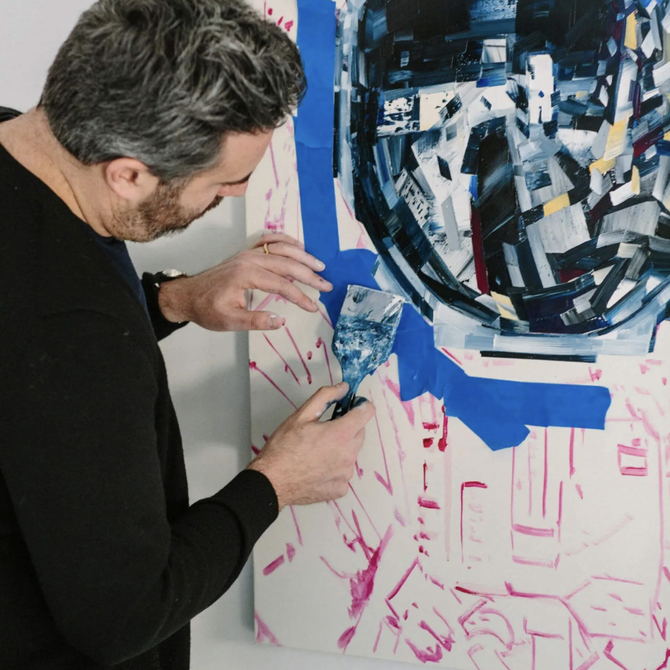 artist concentrating on painting which he has applied blue masking tape to and started filling in with paint in the centre