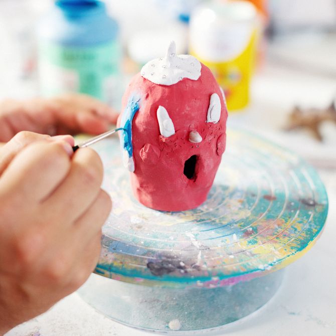 Artist painting blue details onto a small, red clay sculpture in his studio