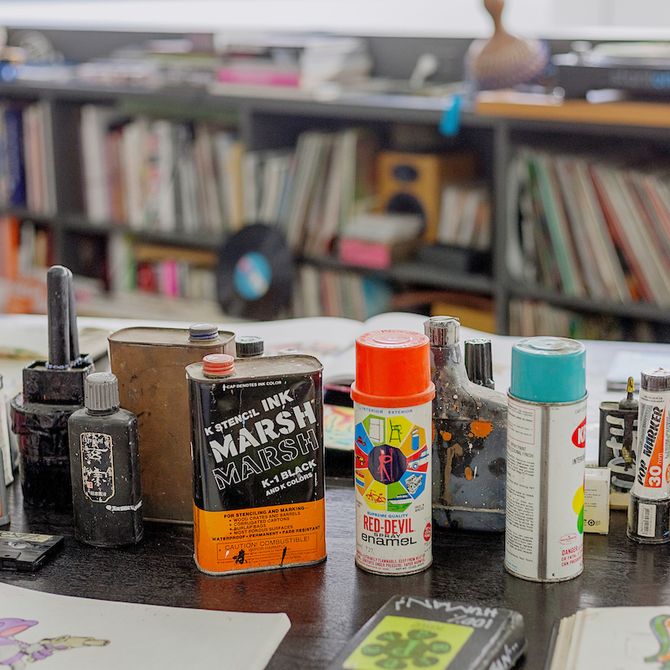 spray paints and various artistic mediums on a table in front of some bookshelves