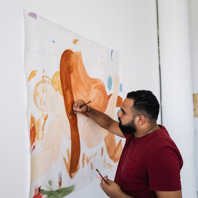 Bony Ramirez painting a white sheet of paper on the wall of his studio