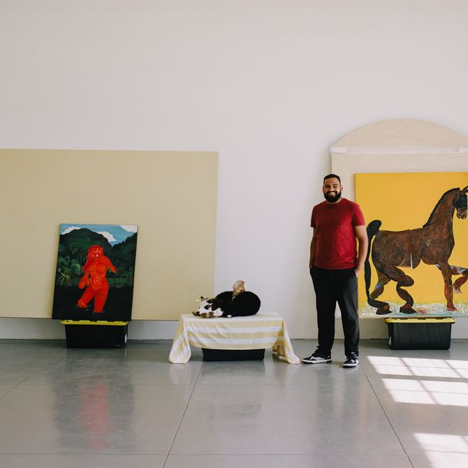 Bony Ramirez standing in his studio with a cow and two paintings