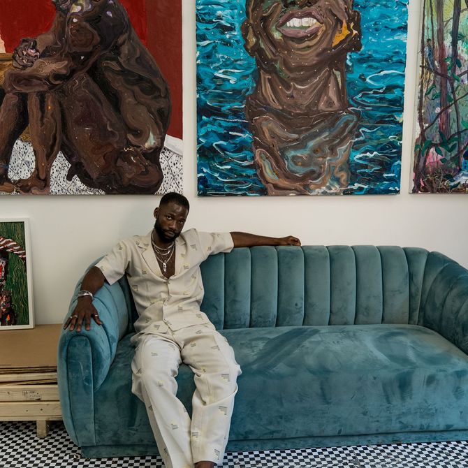 Ludovic Nkoth sat on a blue sofa in his studio with three large paintings hung on the wall behind him
