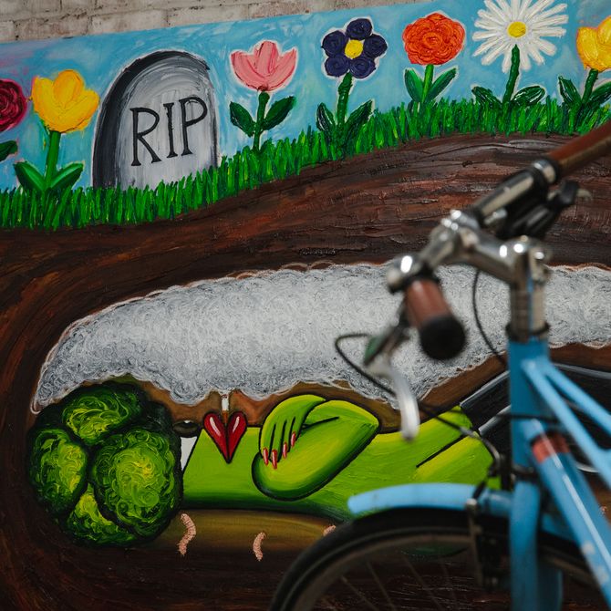 artwork of a broccoli lying in a grave smoking with a bicycle placed in front of it in the artist's studio