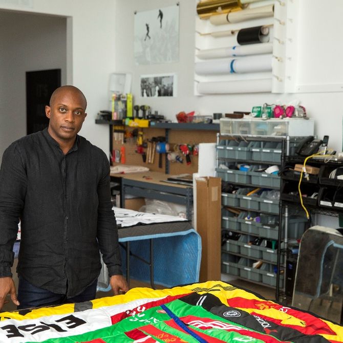 Hank Willis Thomas in his studio standing over a large and colourful tapestry laid on the table before him