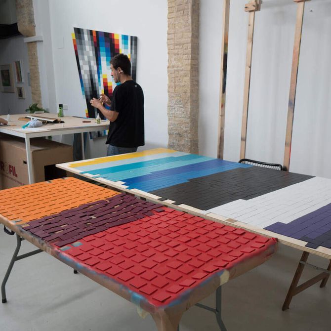 blocks of colours and prints on desktops in the artist's studio with two figures behind them