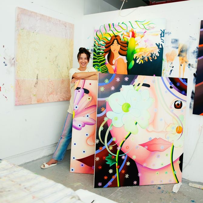 Marcela standing behind a couple of her paintings in the corner of her studio