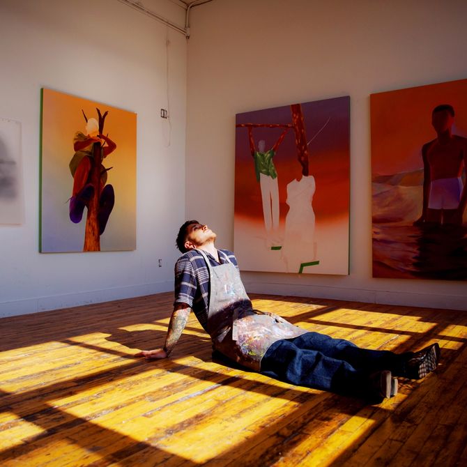Caleb Hahne's sitting on the floor in his studio loft with paintings in the background