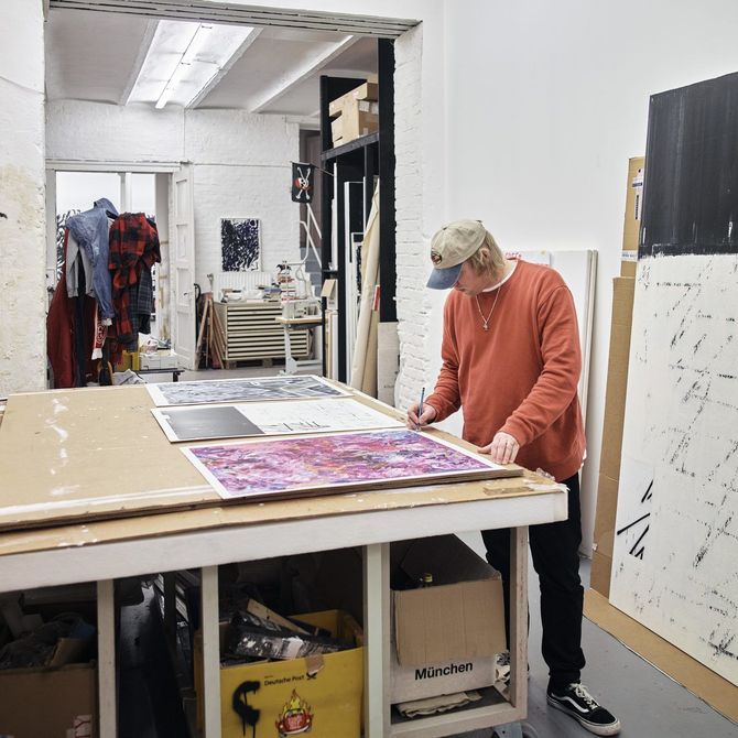 Chris Succo signing artworks that rest on a large table surface in his studio