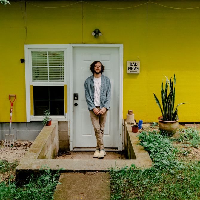 Ryan Travis Christian standing outside the door to his studio, yellow building