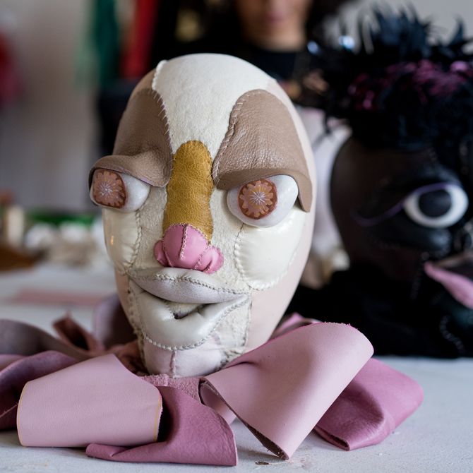 pink, brown and yellow three-dimensional head with visible stitching, placed on a table with other heads