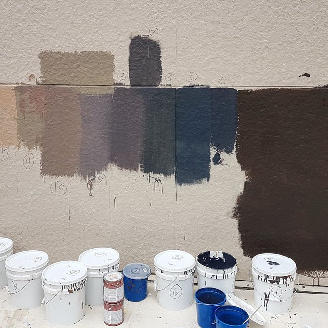 paint pots lined up beneath a white wall with various paint colours sampled on it