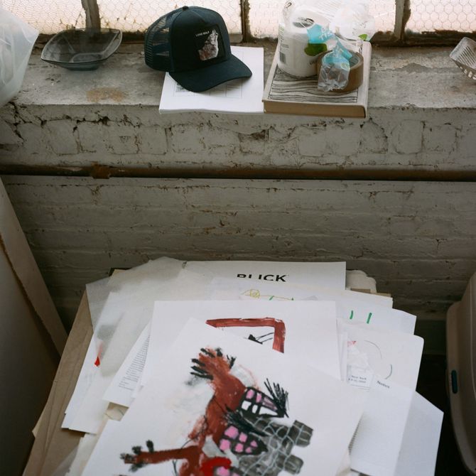 pile of drawings and paintings on white paper by a windowsill in the artist's studio