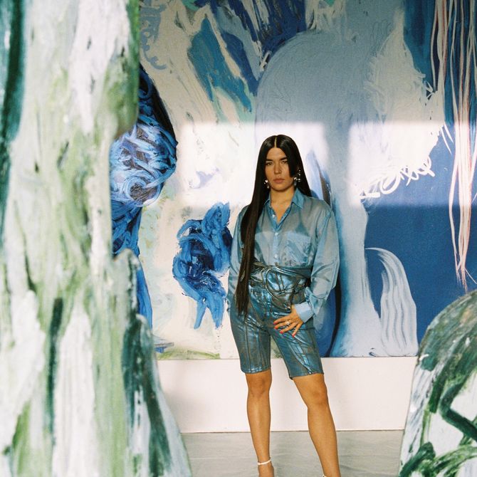 Donna Huanca stood in her studio framed by a green painting and with a large blue abstract painting behind her