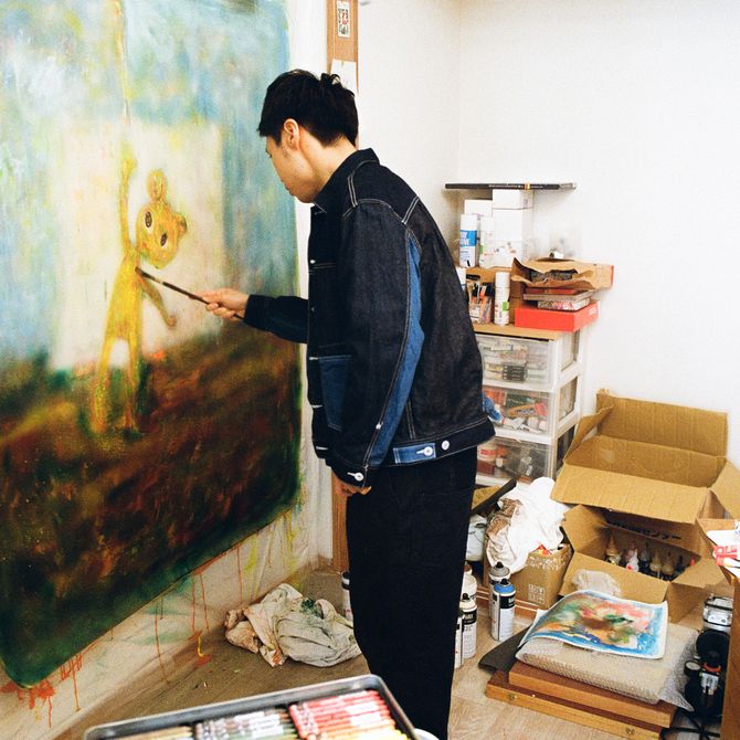 Chen Wei Ting reaching a paintbrush out to a large square painting hung in his studio