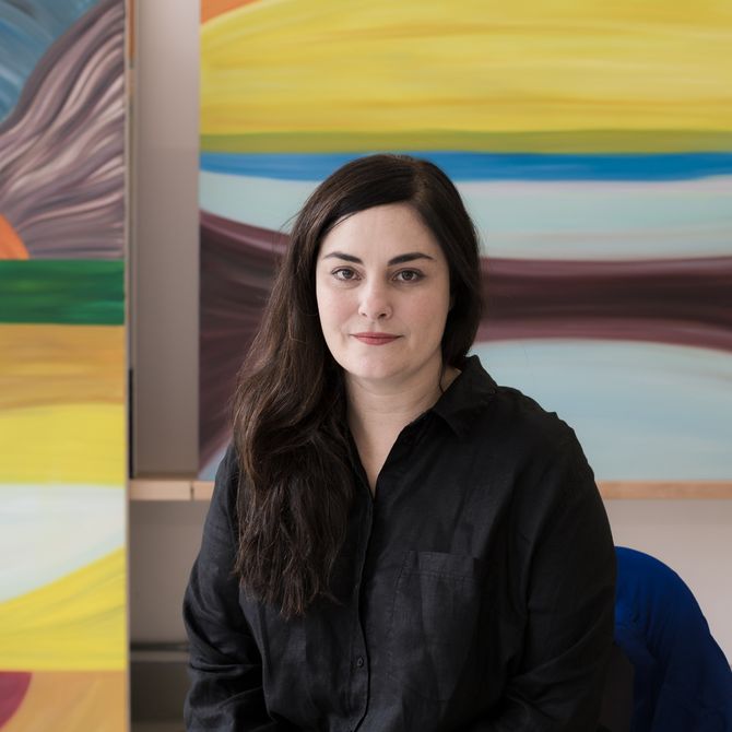 Marina sitting in front of a colourful painting and smiling wearing a black shirt