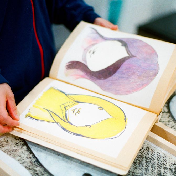 artist Maiko Kobayashi opening one of her sketchbooks with two illustrations of girls portraits