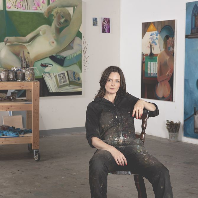 Danielle Orchard wearing a boiler suit with paint stains on it and sat on a chair in her studio