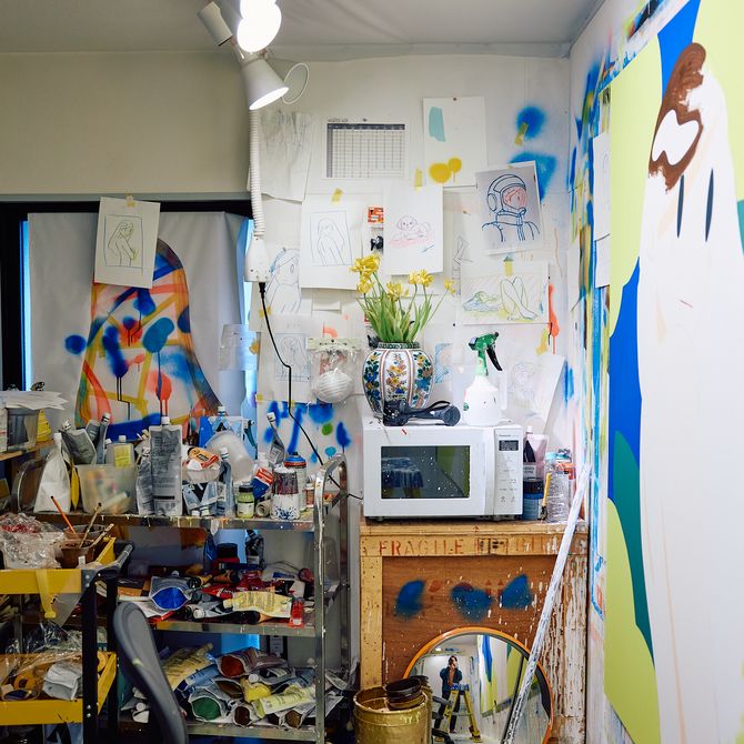 an artist's studio filled with paint pots, a large canvas painting and a microwave