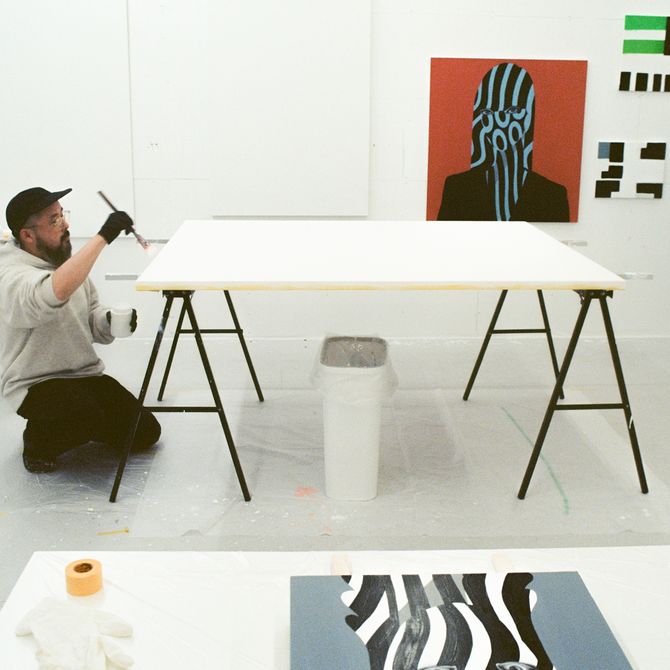 artist Shigeki Matsuyama kneeling on the floor painting a white canvas on a table