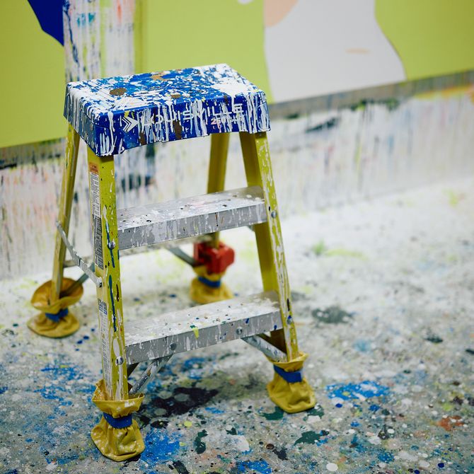 a small stool in the artist's studio covered in white dripping paint