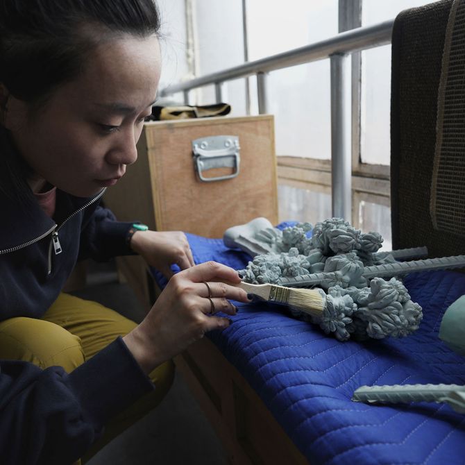 Zhang Ruyi brushing some sculpted objects in her studio
