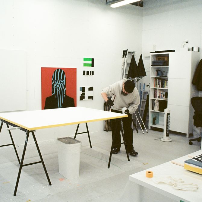 Artist Shigeki Matsuyama bending down to work on a white canvas in his studio