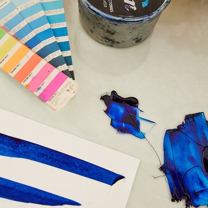 a table with strips of various colours on, next to a piece of paper where various marks have been made with blue paint