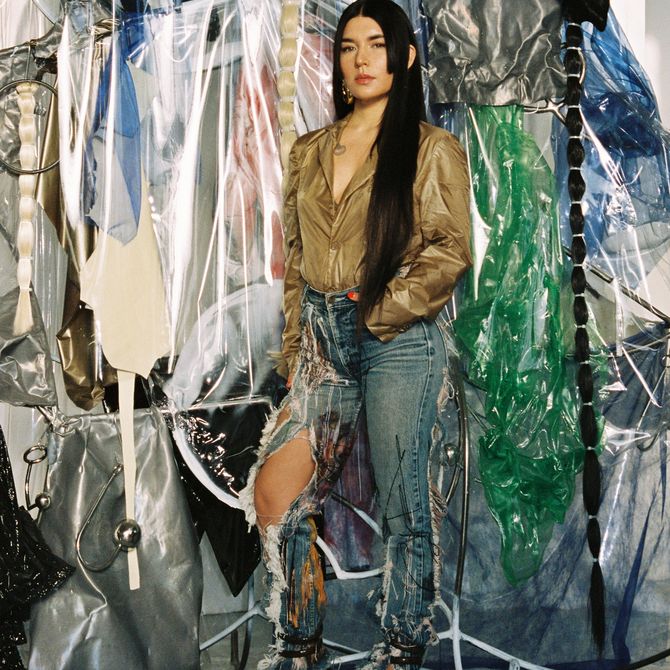 Donna Huanca standing with her hands in her pockets in front of a collection of materials and installations