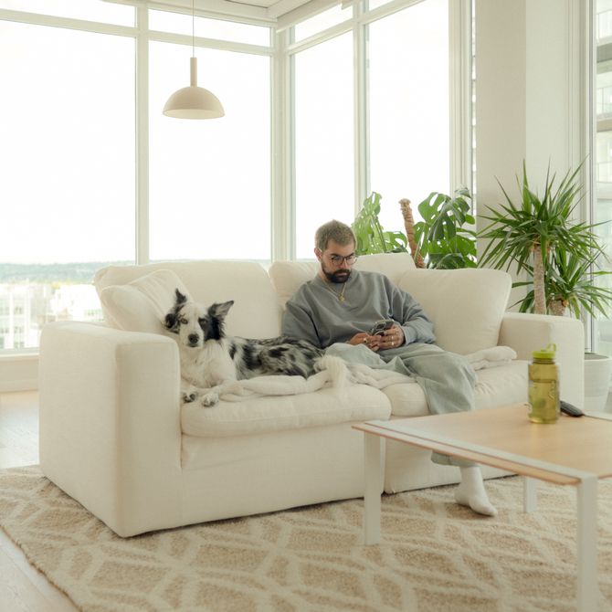 fvckrender, an artist, sitting on a big ecru couch with his black and white dog
