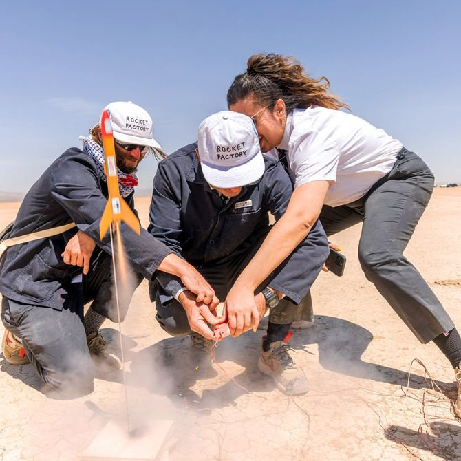 3 people launching a small orange rocket in the desert