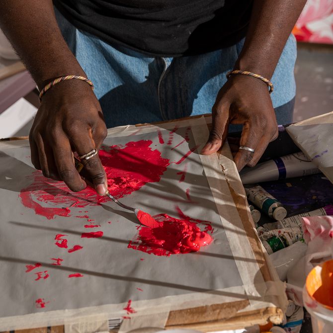 artist dipping a palette knife into a pile of thick red paint on a surface