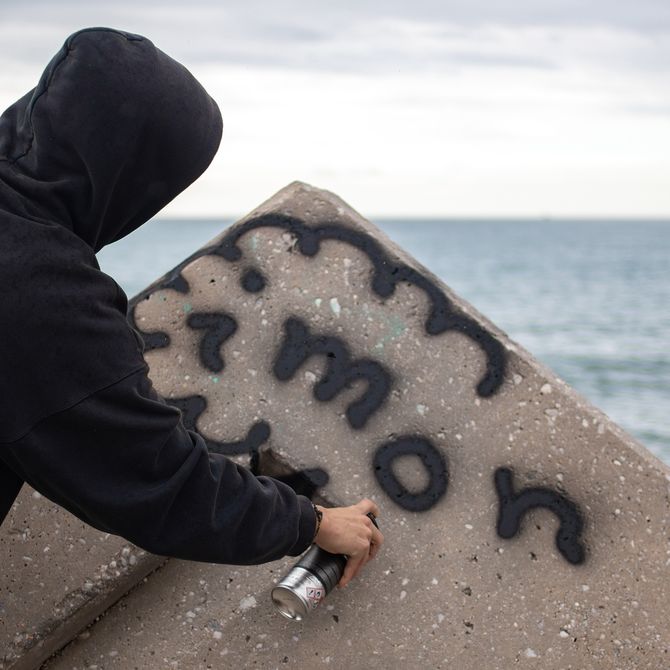 Imon Boy graffiti'ing his name on a concrete slab