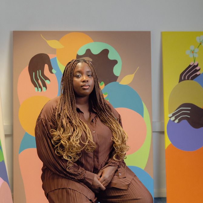 Deborah Segun sitting in front of three of her paintings in a studio