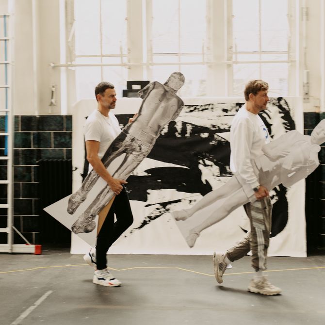 two artists walking whilst holding life-size, photographic cardboard cutouts 