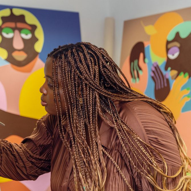 The artist focuses on painting a canvas, with two of her paintings in the background
