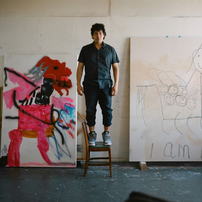 Robert Nava stood on a chair in his studio with canvases either side of him