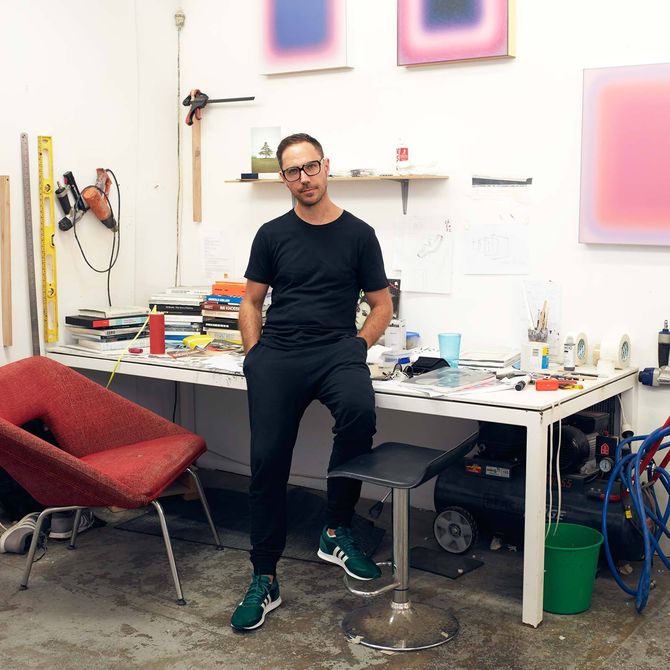 artist Jonny Niesche leans on a desk in his studio