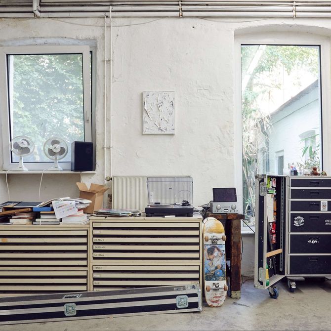 artist's studio filled with storage racks and drawers, a skateboard, technological equipment and a red sofa