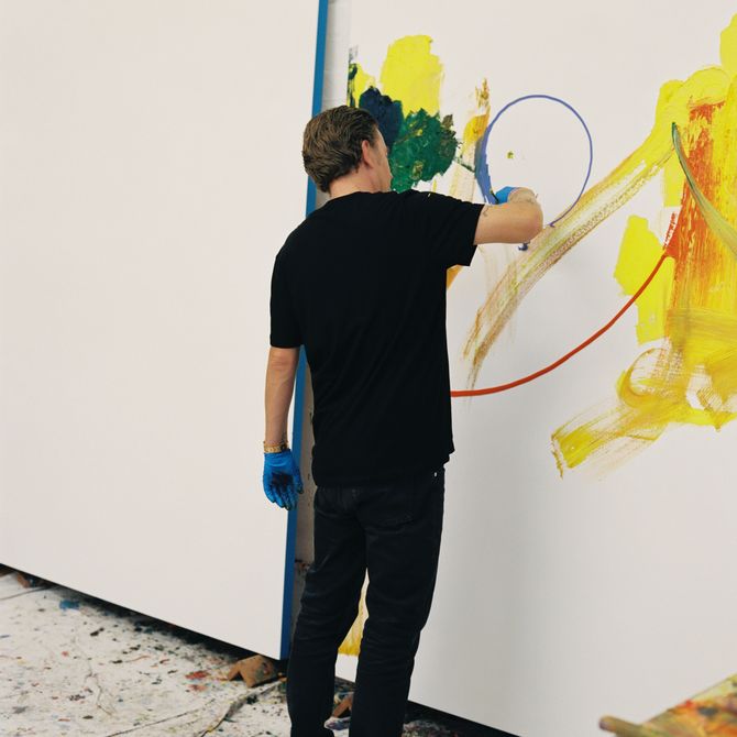 artist facing large painting with black outfit on and blue gloves