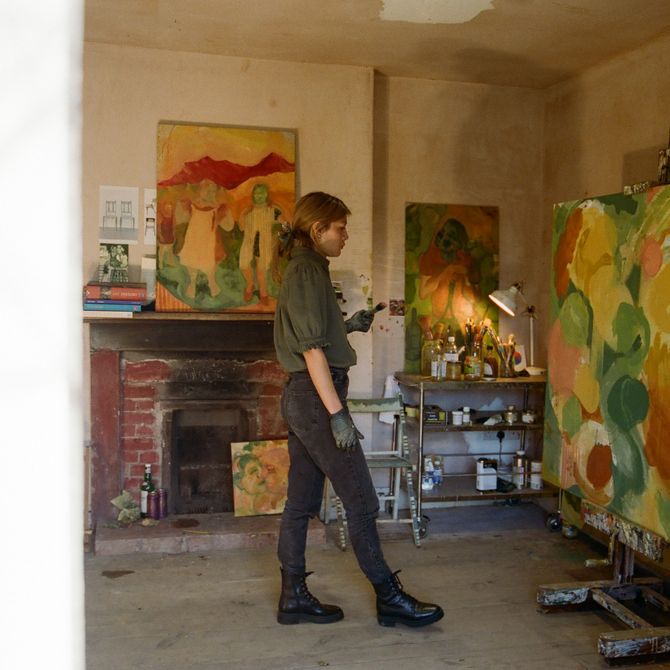 artist viewed from the side whilst she steps back and looks at a large scale painting on an easel 